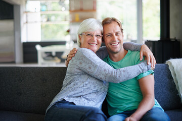 I love having him offer. Portrait of a senior woman embracing her son while sitting on the sofa at home.