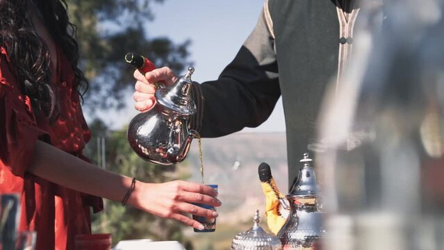 Man pouring fresh Moroccan mint tea for beautiful woman, handheld view