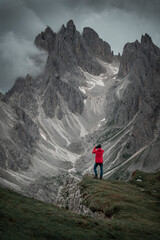 Photographer with camera and red jacket in front of Dolomite Alps at Three Peaks in Italy, low clouds passing by Dolomite mountains.