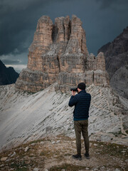 Man taking photos with camera with view to Sasso di Sesto mountains peak in the Dolomite Alps in South Tyrol with dramatic dark sky, Three Peaks Nature Reserve, Italy.