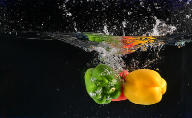 Fototapeta na wymiar Close up of The red, yellow and green bell peppers fell into the water and the water splashed up with black background. Concept for health and vitamins.