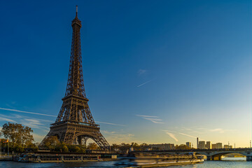 Fototapeta na wymiar Touristic Cruise at Eiffel Tower in Paris at Golden Hour Sunset With Blue Sky