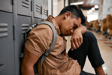 A young South East Asian student leans his head on knees on university campus