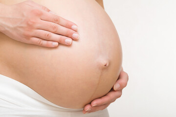 Young adult pregnant woman hands touching big naked belly. Showing shape. Pregnancy concept. Expectation time. Closeup. Isolated on light gray wall background.