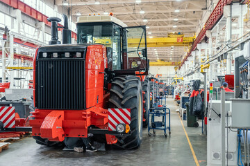 Big red harvester or tractor in process of being assembled on production line at factory for...
