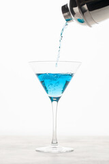 Blue Hawaii  cocktail with blue curacao liqueur, vodka and soda. Pouring a blue cocktail to a glass martini from shaker