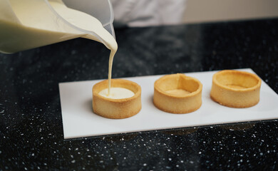 The chef pouring custard cream in the tartlets. Dessert, culinary and confectionery concept.