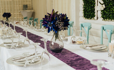 Wedding ceremony. The chairs and table for guests, served with purple flowers in vases and table covered with a white tablecloth.