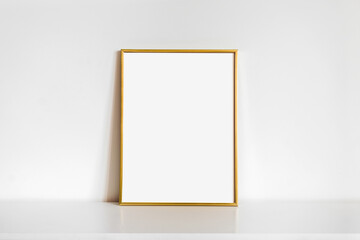 Empty gold vertical frame mockup on white wall background. Template for artwork, painting, photo or...