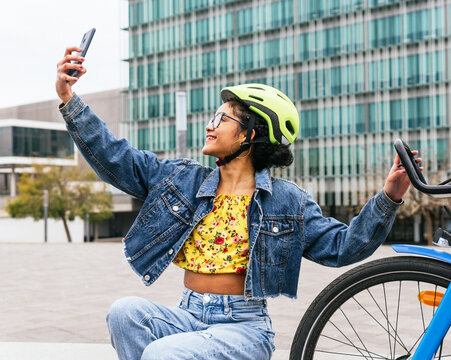 Ethnic lady taking self portrait on smartphone near bicycle on urban street