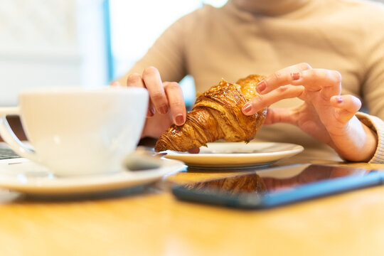 Woman eating croissant with coffee in cafe