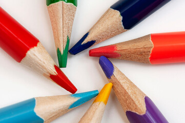 Several multi-colored pencils are arranged in a circle on a white background. Close-up macro shot.