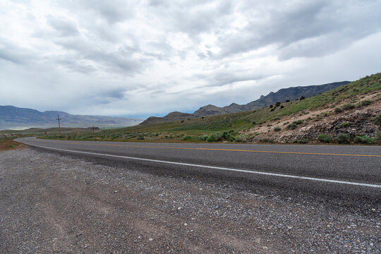 beautiful landscape Horizontal photo of Hwy 50 in Nevada desert with blue and white sky threatening to storm Black top road winding between mountains, green grass fading off to the photograph horizon
