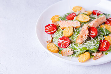 Caesar salad with red fish (salmon, trout), cherry tomatoes, croutons, parmesan cheese and romaine. Traditional American dish. Copy space. Close-up, selective focus.