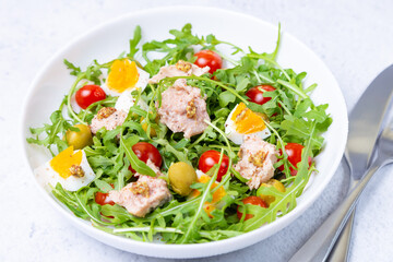 Salad with tuna, arugula, tomatoes, olives and eggs in a white plate. A traditional dish. Close-up.