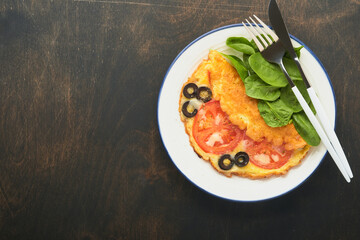 Omelette with tomatoes, black olives, cottage cheese and green spinach herbs on white plate on old wooden rustic dark background. Delicious breakfast. Healthy breakfast food. Top view.