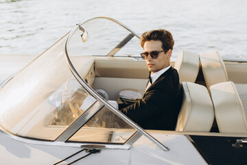 Business portrait of young man in suit and sunglasses posing on a yacht in a daylight sun