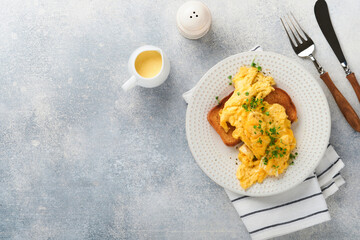 Scrambled Eggs. Fluffy and Buttery scrambled eggs on bread with microgreen radish and hollandaise sauce on white plate over white wooden background. Homemade breakfast or brunch meal. Top view.