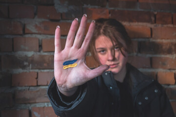 The hand of a girl in front of the face with a painted yellow-blue flag of Ukraine, peace in...