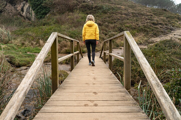 A woman crosses a wooden bridge in the countryside. The woman crosses a bridge leaving behind her former life and beginning the path of her new life and her own destiny.