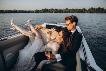 Man in a black suit and sunglasses hugs a woman on a yacht on a sunny day. Couple drinking...