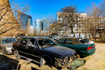 Wreck cars scrapyard with skyscrapers of modern Wola business district of Warsaw, Poland in background