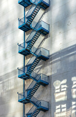 Blue emergency fire stairs metal construction aside plain grey concrete wall of a modern utility...