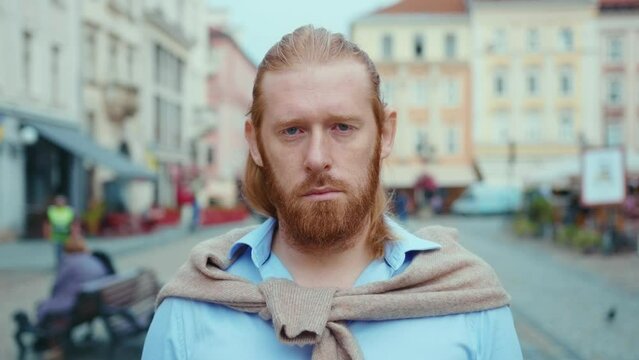 Closeup portrait of attractive redhead bearded guy looking serious into camera in city center. Urban background. Caucasian businessman. Confidence.