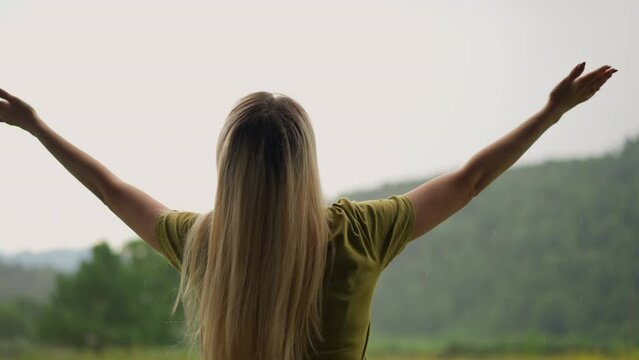 Woman raise hands up happy of warm rain against green hill