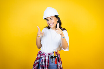 Young caucasian woman wearing hardhat and builder clothes over isolated yellow background pointing...