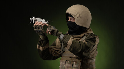 a soldier in military clothes with a weapon launches a small unmanned quadcopter for reconnaissance on a dark background