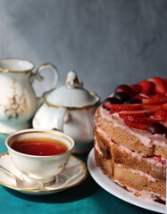 Vintage cup with black tea, strawberry cake and fresh berries on textured background. Sweet food still life. Birthday cake close up photo. 