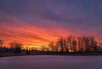 Fototapeta na wymiar Vibrant Sunrise Glowing Over A Frozen Park Lake