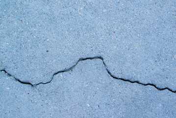 a crack on the asphalt with a curved line of bluish-grayish color