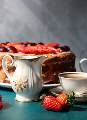 Retro tableware on a table. Cup of tea, milk jug, fresh berries and strawberry cake. Textured background with copy space. 
