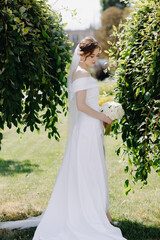  Bride in a white dress and a bouquet of white peony posing in the park