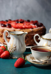 Retro tea party. Beautiful white and gold cup, sugar bowl, milk jug and strawberry cake. Sunny morning photo. Sweet food on a table. 