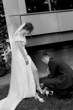 The groom helps the bride to put on her shoes. Black and white photo