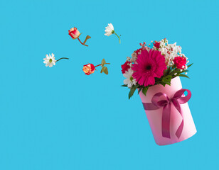 Pink gift box with various spring flowers on blue background. Flying flowers from the box. Mother's Day idea.