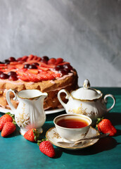 Retro tableware on a table. Cup of tea, milk jug, fresh berries and strawberry cake. Textured background with copy space. 