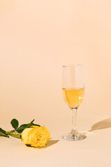 Vintage style concept with wine glass and yellow rose flower on beige background. Spring minimal concept. Copy space.
