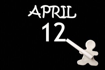 A small white plasticine man writing the date 12 April on a black board. Business concept. Education concept.
