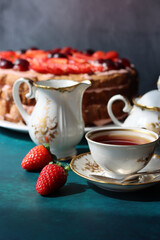 Retro tableware on a table. Cup of tea, milk jug, fresh berries and strawberry cake. Textured background with copy space. 