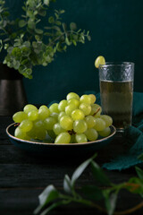 Juicy green grape on the plate with glass of grape juice close up