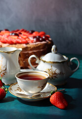 Retro tea party. Beautiful white and gold cup, sugar bowl, milk jug and strawberry cake. Sunny morning photo. Sweet food on a table. 