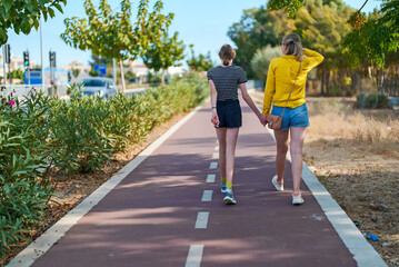 Mom and her daughter walk along the footpath in summer.