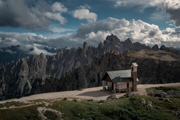 Fototapeta na wymiar Chapel Cappella degli Alpini in front of mountain panorama in Dolomite Alps at Three Peaks in Italy, clouds in sky.