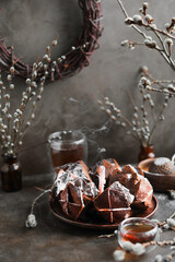 Chocolate sponge cake with spices and powdered sugar on a wooden stand. Still life with chocolate dessert and willow branches in dark colors