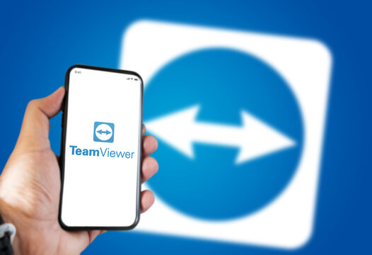 hand holding a phone with the Teamviewer mobile app on the screen with the Teamviewer icon blurred on a blue background