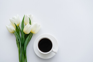 top view of tulips near cup with coffee on saucer on white.